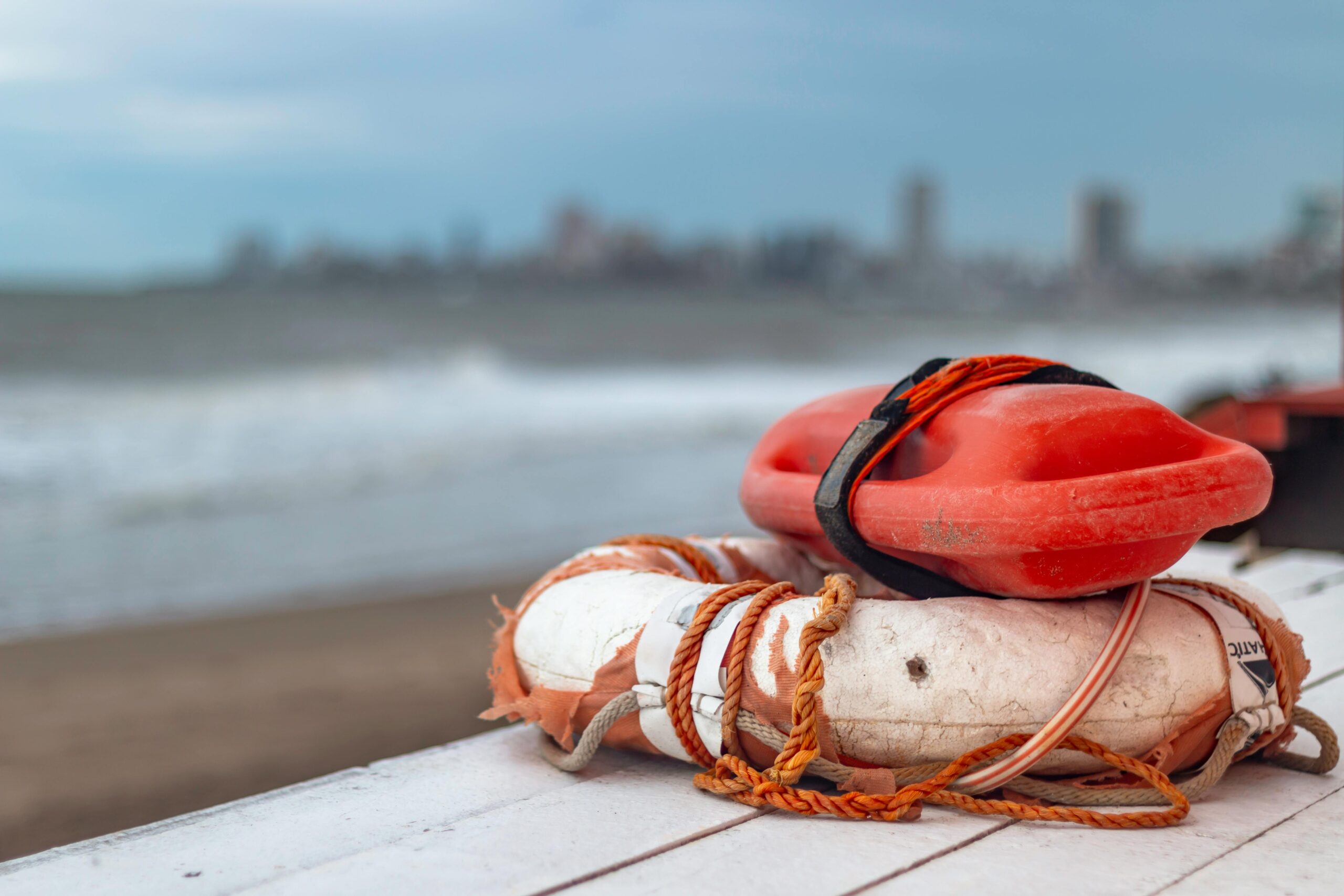 Close-up of a lifebuoy and rescue float on Mar del Plata beach in Argentina, with city skyline in the background.