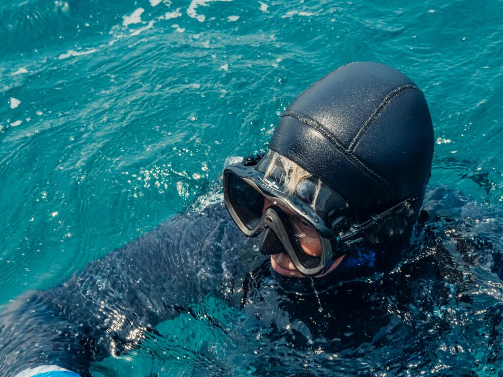 Close-up of a scuba diver in a wetsuit wearing goggles in the ocean.